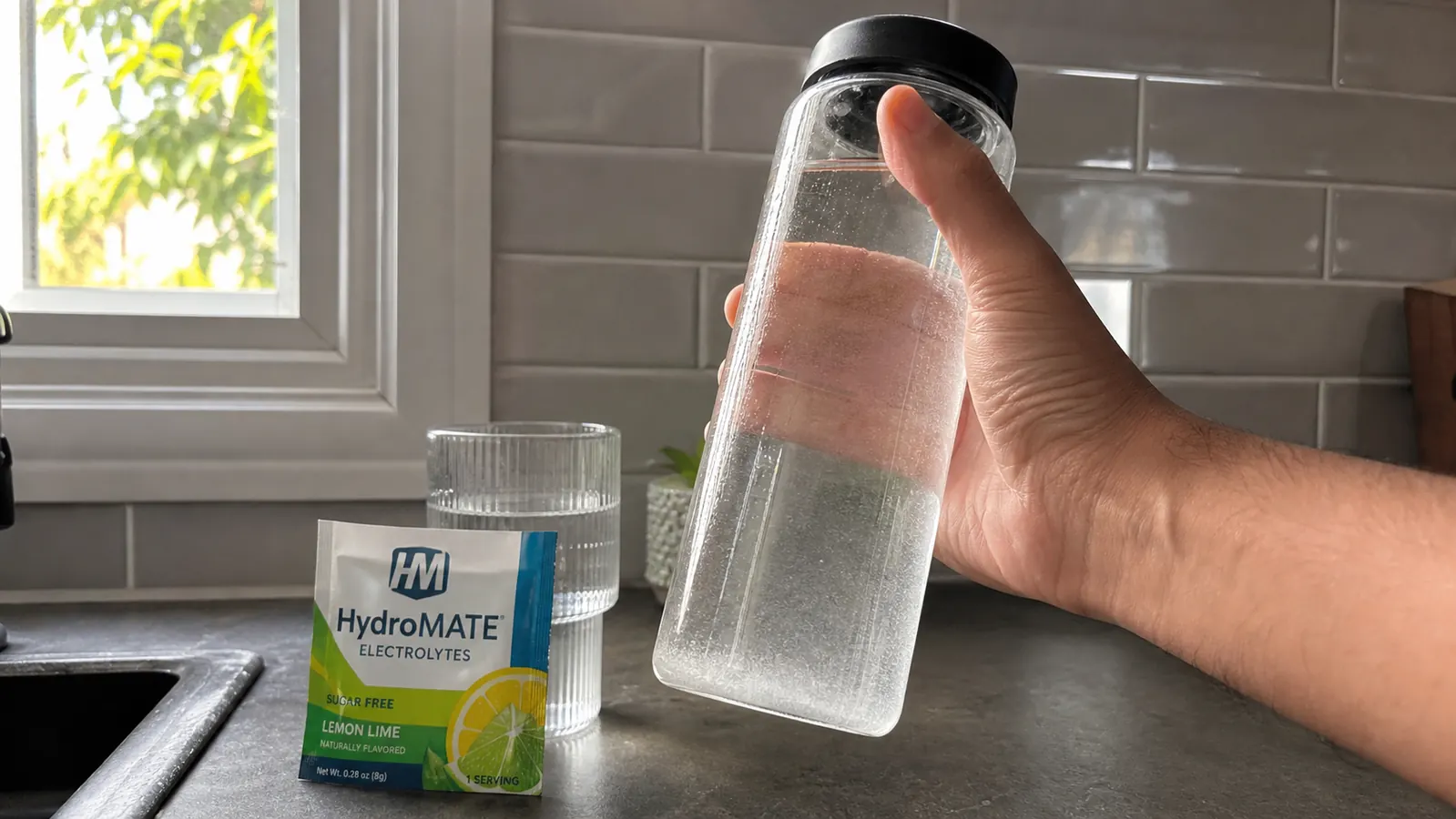 Close-up of hands shaking a water bottle with an electrolyte packet mixed in, checking for clumping at the bottom