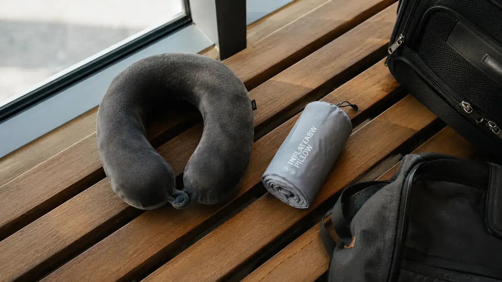 Two travel pillow styles laid side by side on an airport bench, a memory foam neck pillow and a deflated inflatable pillow